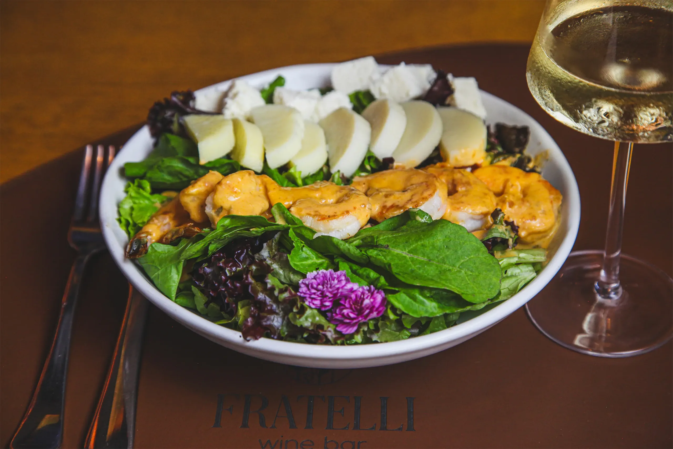 Salada com camarões grelhados, palmito, queijo fresco e folhas verdes no Fratelli Wine Bar, acompanhada de vinho branco