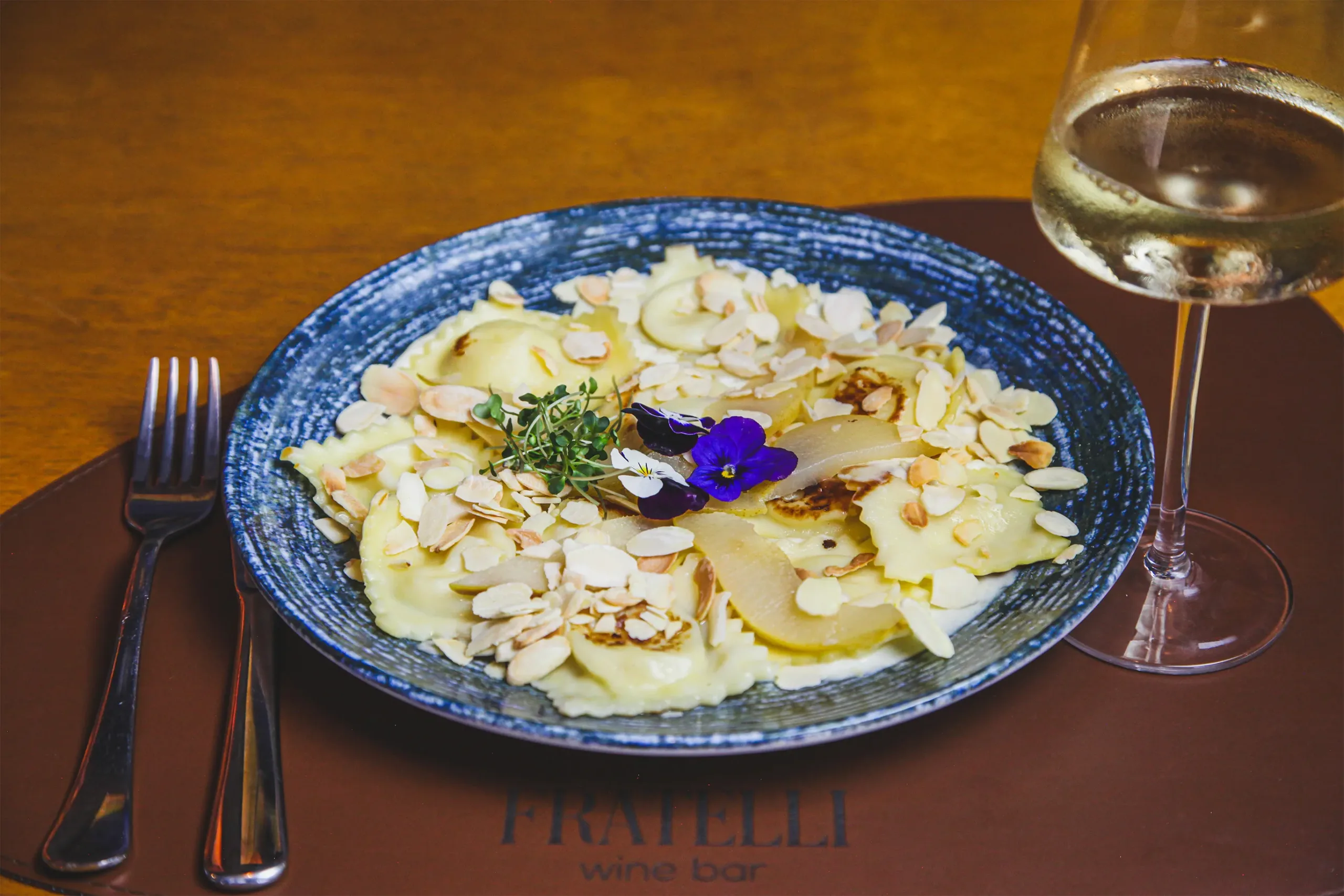 Ravioli artesanal com amêndoas laminadas e peras no Fratelli Wine Bar, servido com vinho branco
