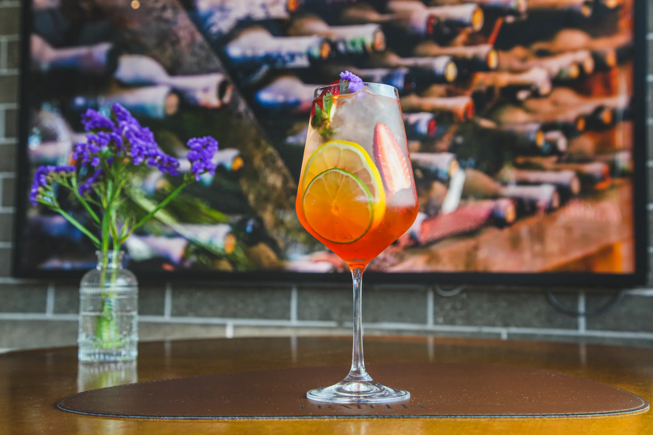 Drink colorido com frutas cítricas, morango e flor comestível servido em taça no Fratelli Wine Bar em Holambra.